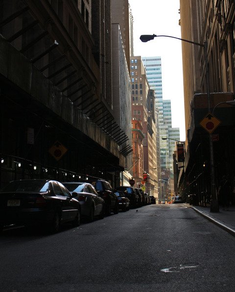 A narrow street of parked cars between Manhattan towers