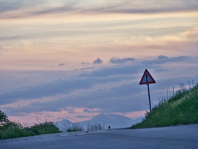 A warning sign on a hilltop road at dusk, mountains behind